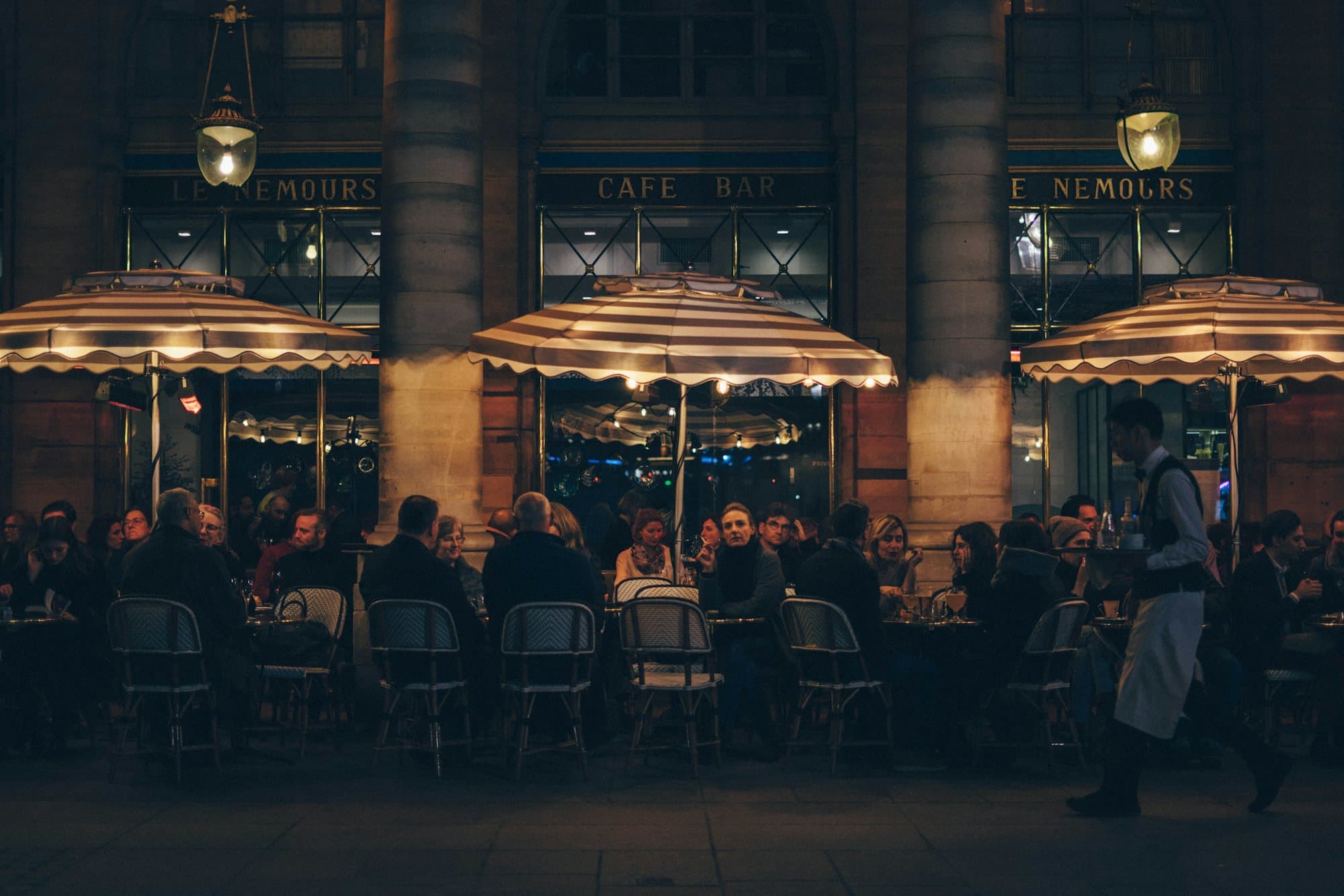 Terrasse de café animée en soirée, service à plein régime