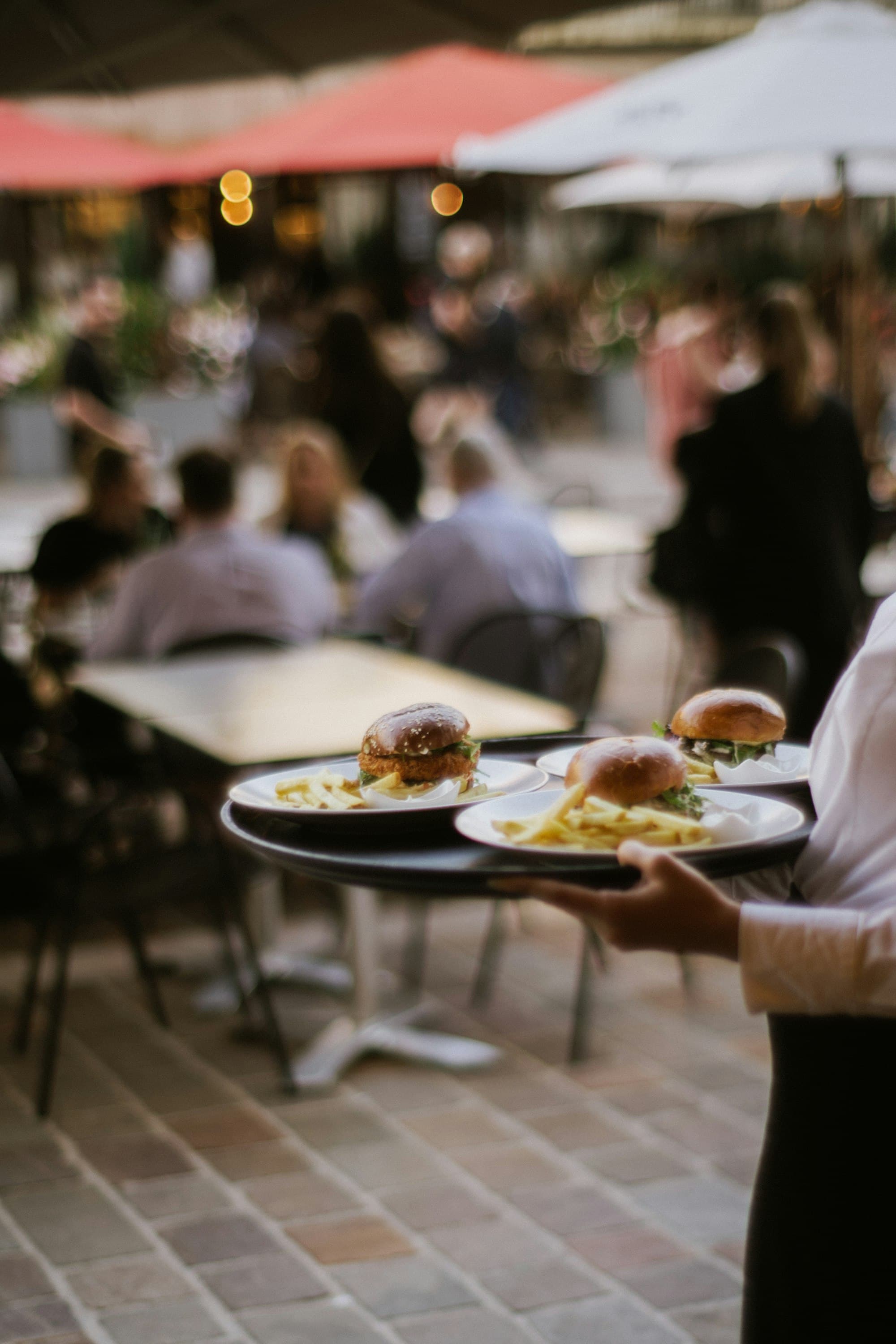 Serveur portant un plateau de plats sur une terrasse de restaurant ensoleillée